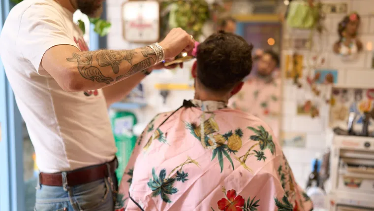Tattooed barber working a fresh cut in a tropical cape at Tallboys, Brighton