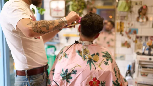 Tattooed barber cutting hair in a tropical cape at Tallboys